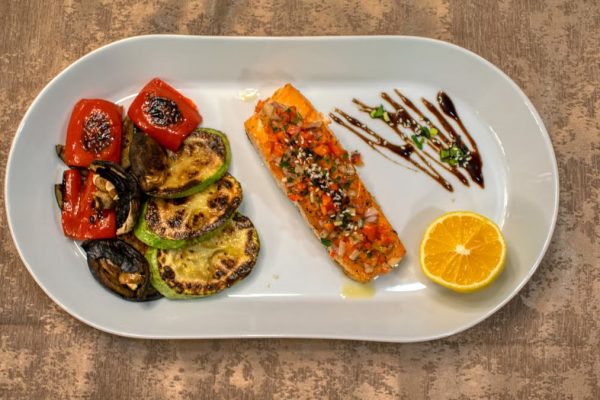 Gourmet grilled salmon served with roasted vegetables and lemon slice on a white plate.
