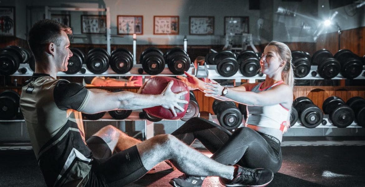 A couple engaged in a fitness session using a medicine ball in a gym environment.