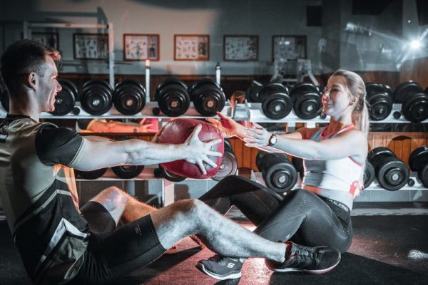 A couple engaged in a fitness session using a medicine ball in a gym environment.